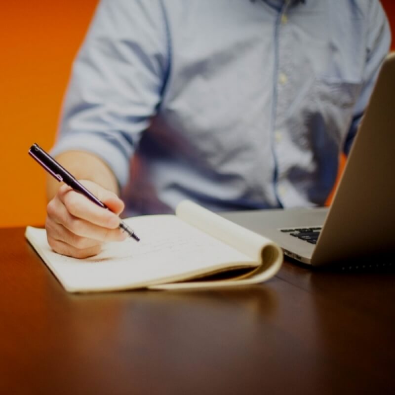 man at laptop writing in notebook